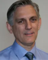 Professional man with gray hair in a blue shirt and tie, smiling against a neutral background.